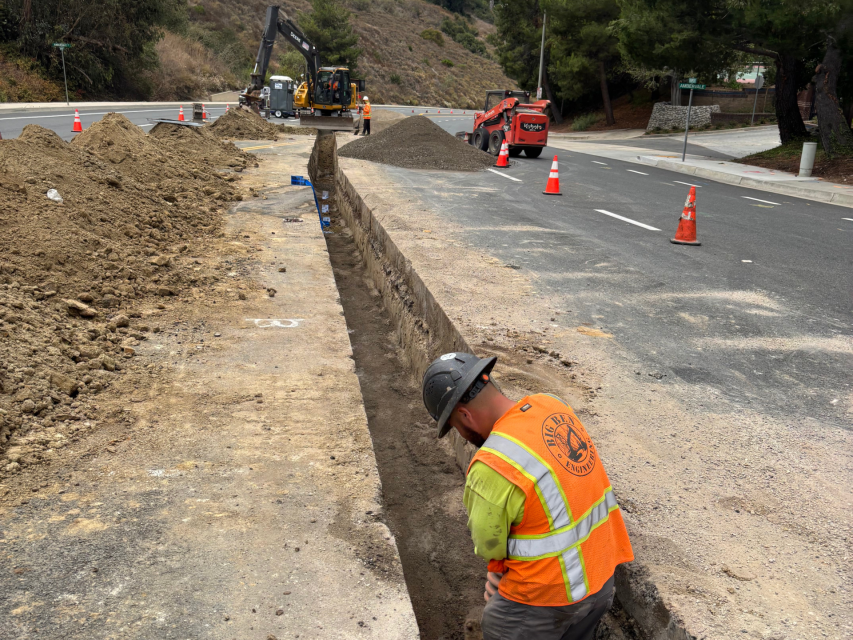 A worker with a hardhat placing water pipe in a trench.