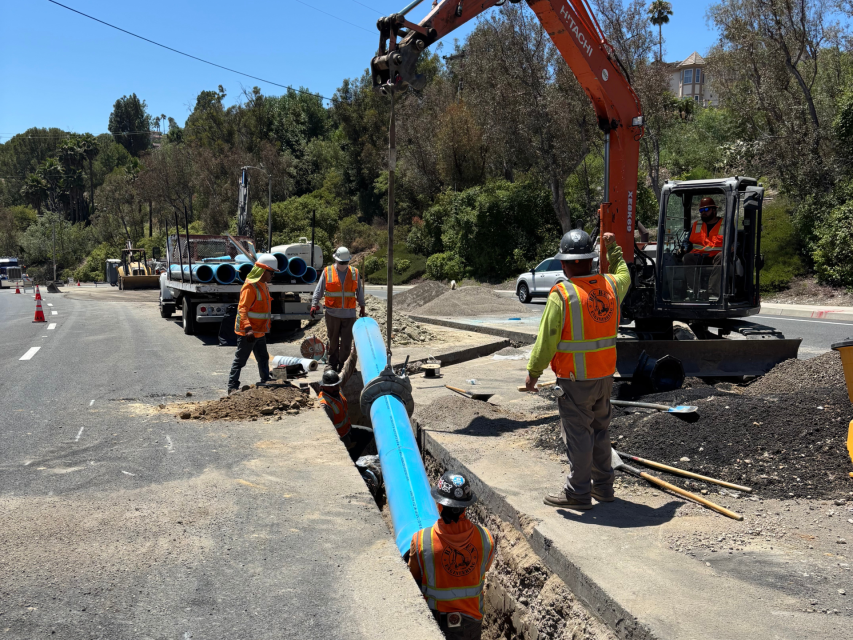 A group of workers in hard hats using an escalator to lay new water pipe in the ground.